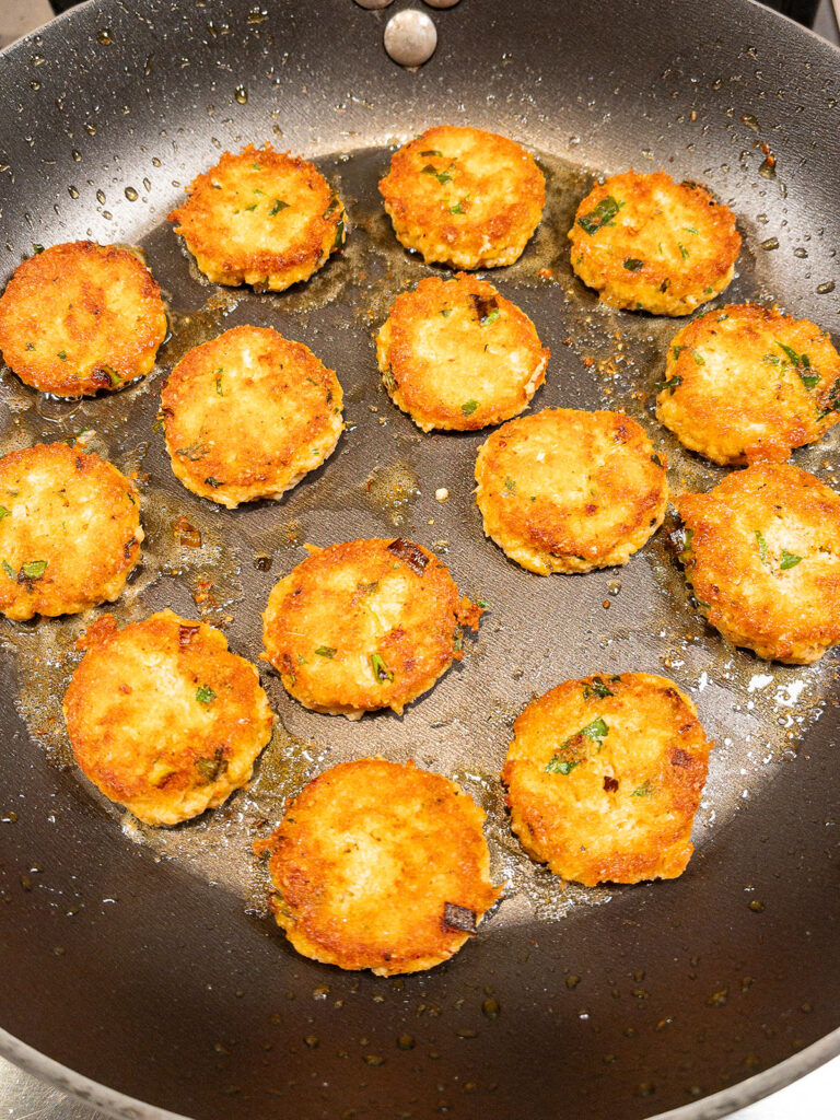 Keto crab cakes being seared in a pan with fresh herbs
