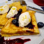 Plate of keto crepes topped with lemon zest and whipped cream garnished with blueberry fruit compote sauce featured image