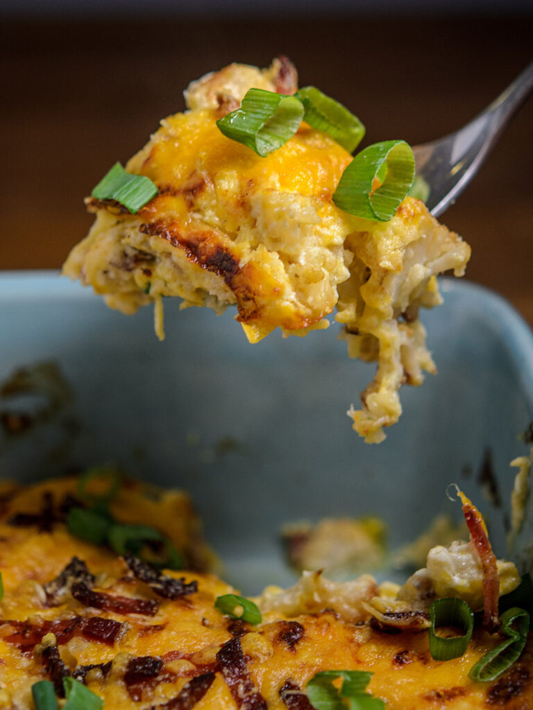 Close up of loaded cauliflower bake suspended on a fork over the baking dish