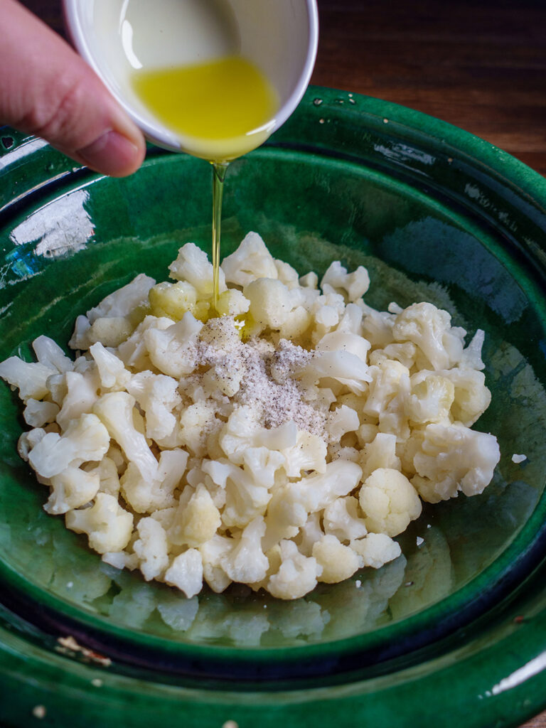 Bowl of cauliflower with ingredients being added for the loaded cauliflower bake