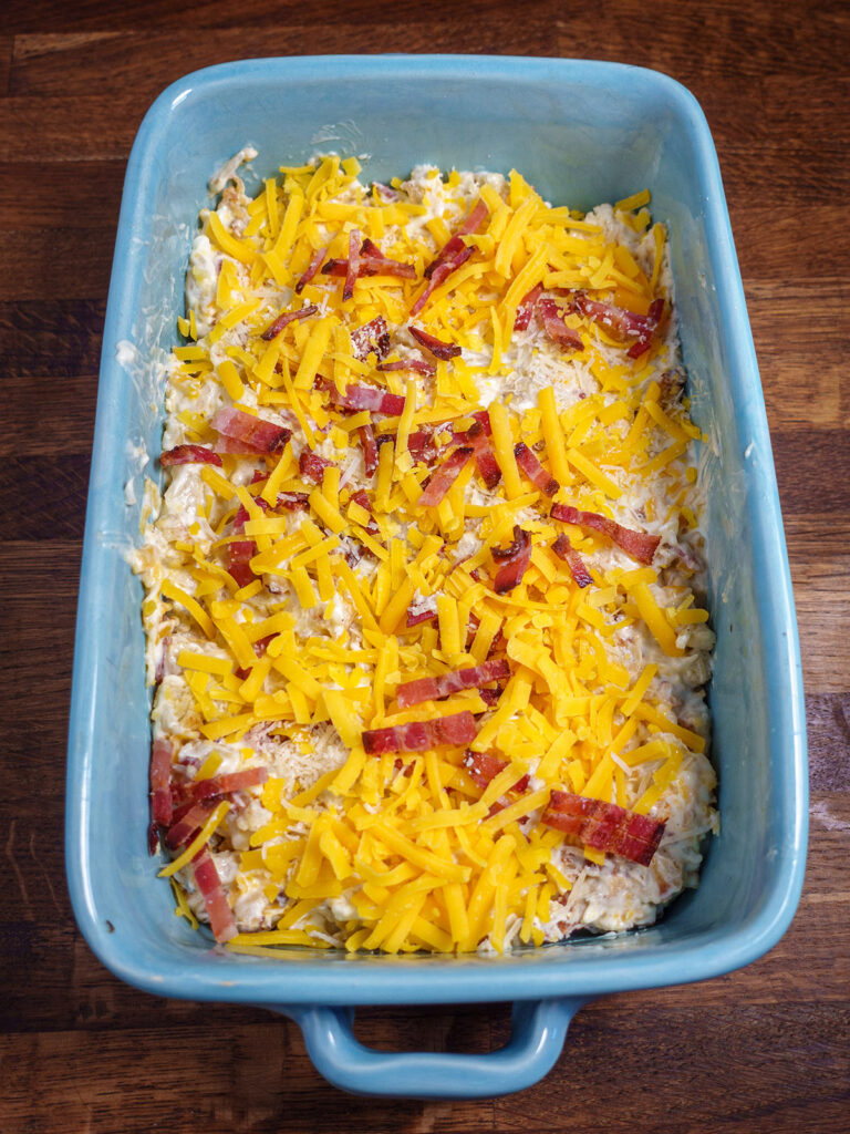 Baking dish full of mixed ingredients for loaded cauliflower bake topped with bacon and cheese