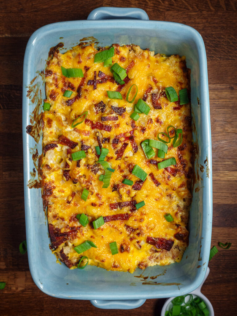 Loaded cauliflower bake in a baking dish topped with scallions