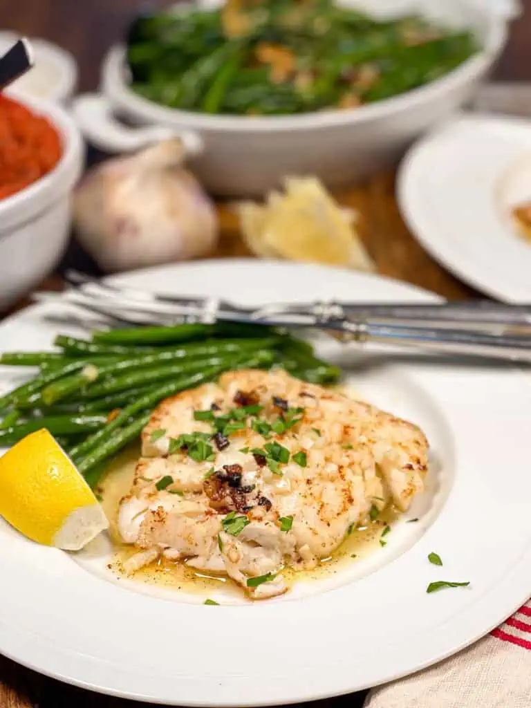 Pan seared cod with green beans and fresh herbs served on a white plate