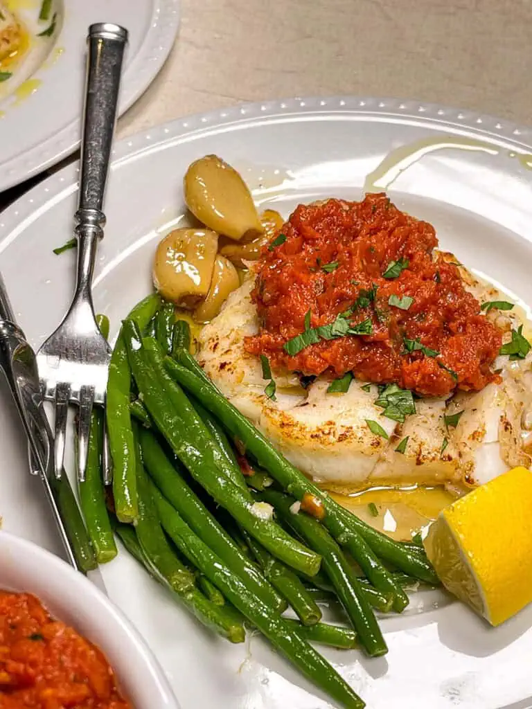 Plate of pan seared cod topped with fresh herbs and served with keto roasted garlic