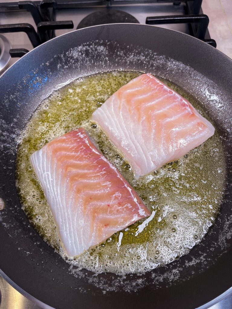 Raw cod searing in a pan in preparation for pan seared cod