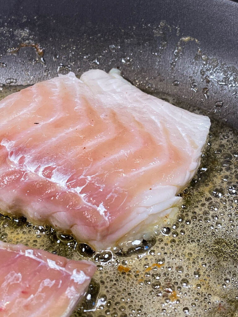 Close up of raw cod searing in a pan in preparation for pan seared cod