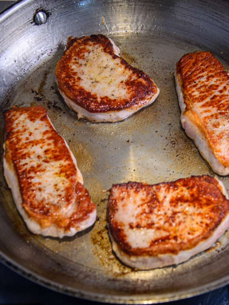 Pan with cooked and seared pork chops for smothered pork chops
