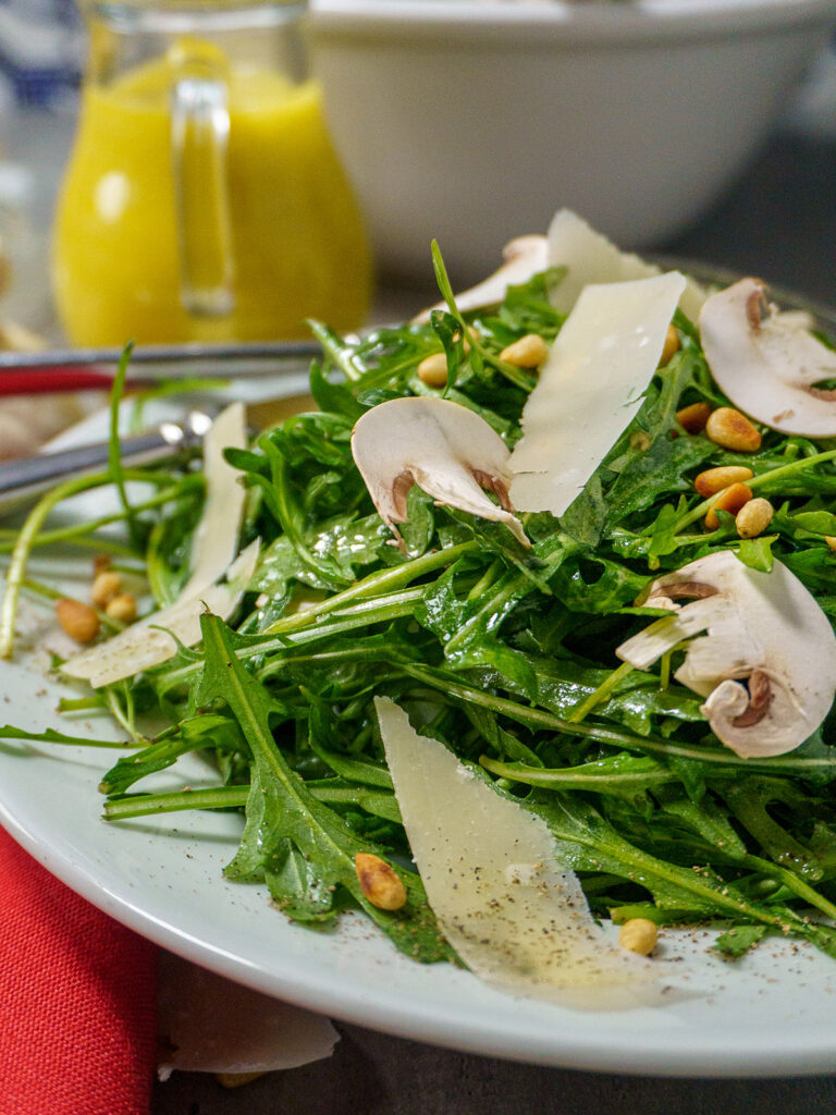 Arugula mushroom salad with toasted pine nuts and shredded parmesan cheese on a white plate