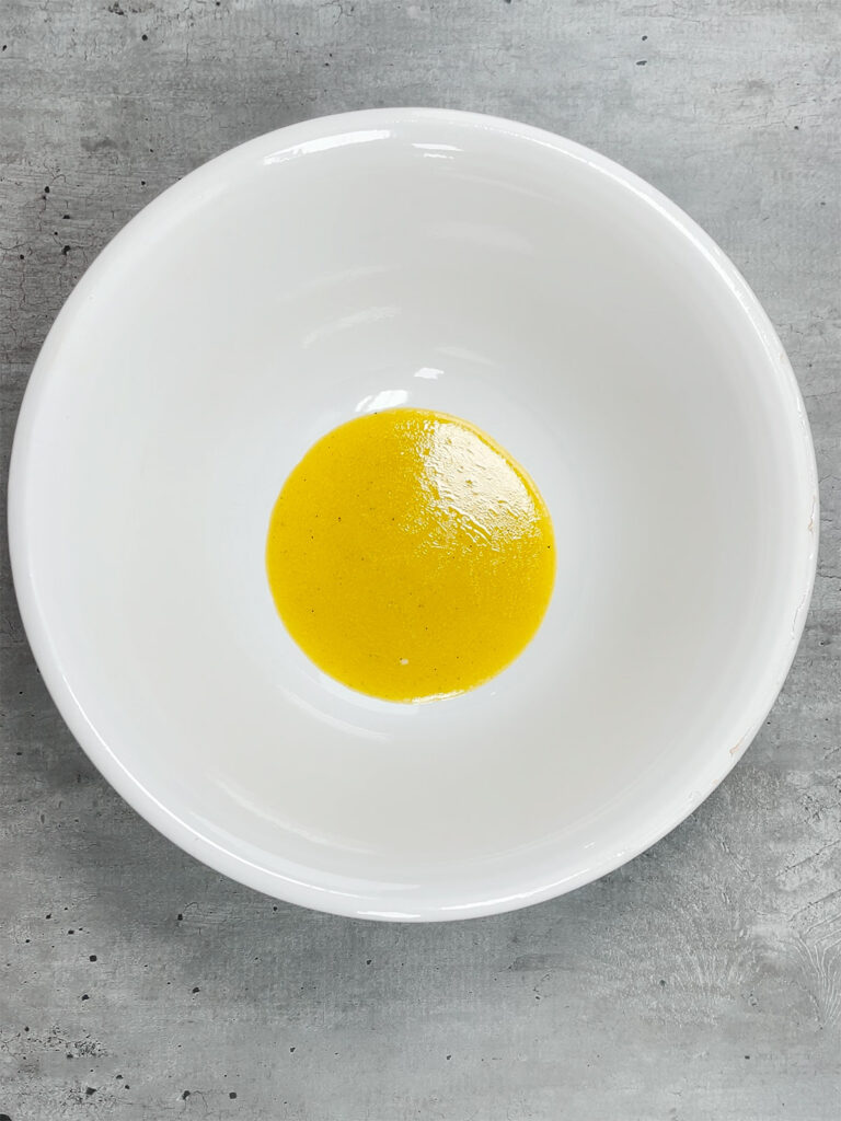 Adding vinaigrette in the bottom of a white salad bowl on a gray background
