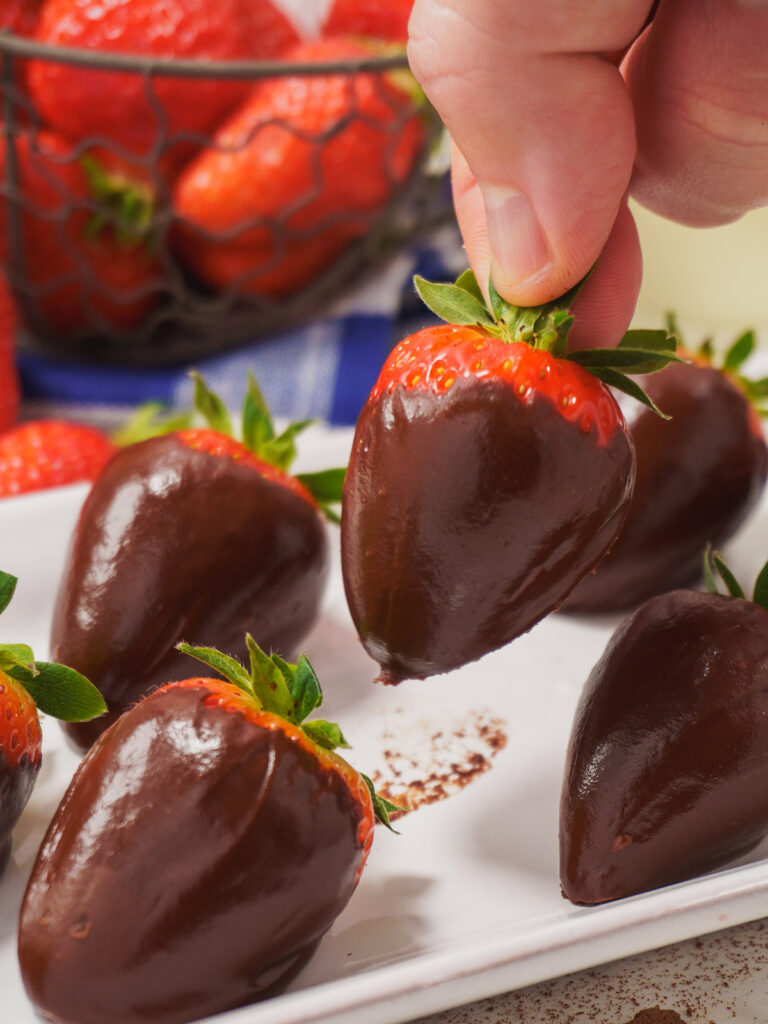 close-up-of-a-strawberry-covered-in-chocolate-held-in-a-hand-above-a-plate
