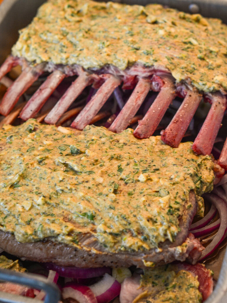 coating a rack of lamb with herb mustard and getting ready to roast
