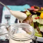 Spoonful-of-creamy-ranch-dressing-above-a-jar-with-a-salad-in-the-background
