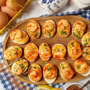 Overhead-view-of-a-wooden-platter-full-of-Cajun-Shrimp-Deviled-Eggs-with-spices-and-a-basket-of-eggs-in-the-background