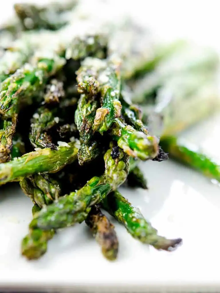 A close-up shot of grilled asparagus spears, charred to perfection, and topped with a light dusting of Parmesan cheese.