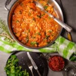 A vibrant skillet of sun-dried tomato chicken, garnished with fresh spinach and sprinkled with pine nuts. The rich, creamy tomato sauce envelops the tender chicken pieces.