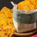 Crispy keto cheese chips with bacon bits served in a fabric-lined basket, with additional chips scattered on a wooden board.