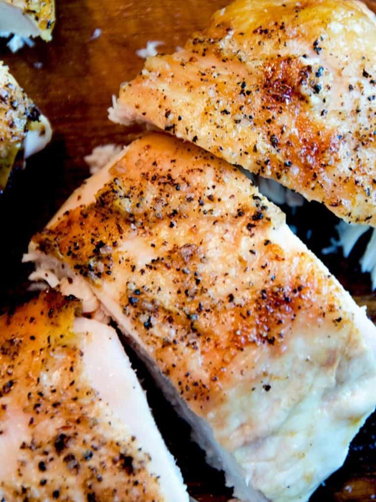 Close-up of golden-brown, seasoned chicken breast slices on a wooden cutting board.
