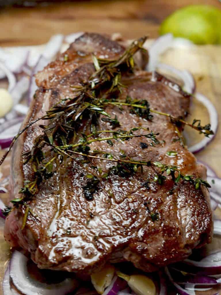 A close-up of a cooked beef chuck roast garnished with rosemary and thyme, with the roast partially submerged in broth.