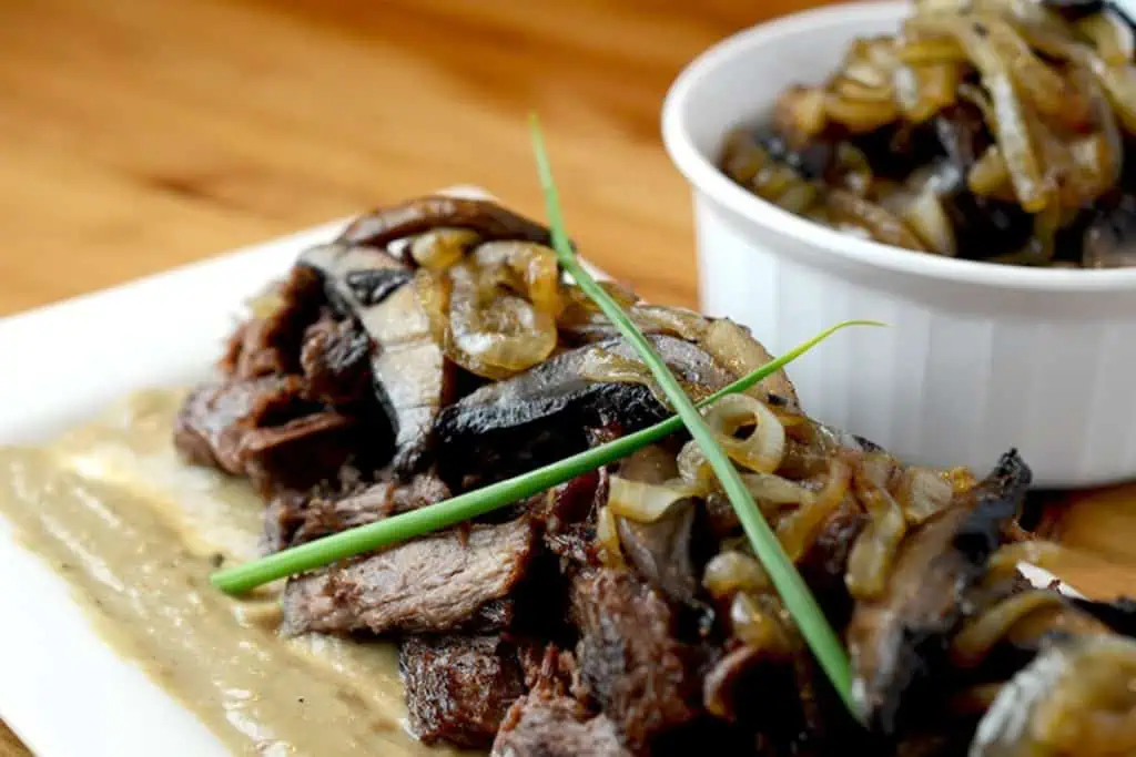 A boneless beef chuck roast in a pan, garnished with rosemary and thyme sprigs, with the stove in the background.