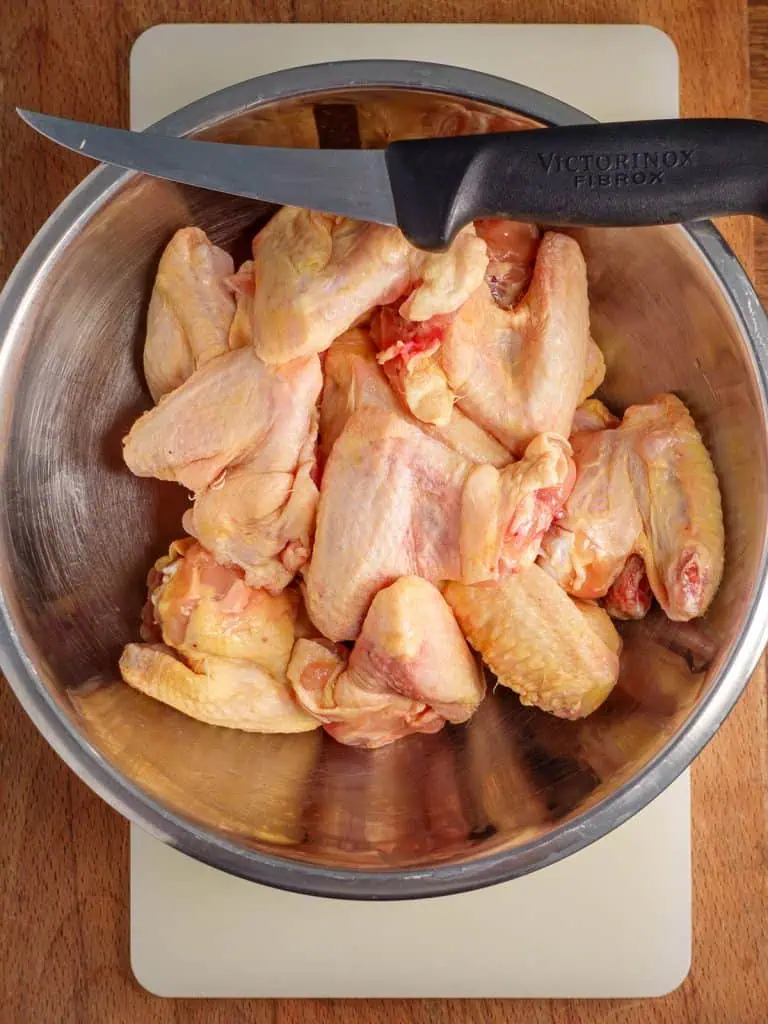 A bowl of raw chicken wings with a knife on the side, ready for preparation.