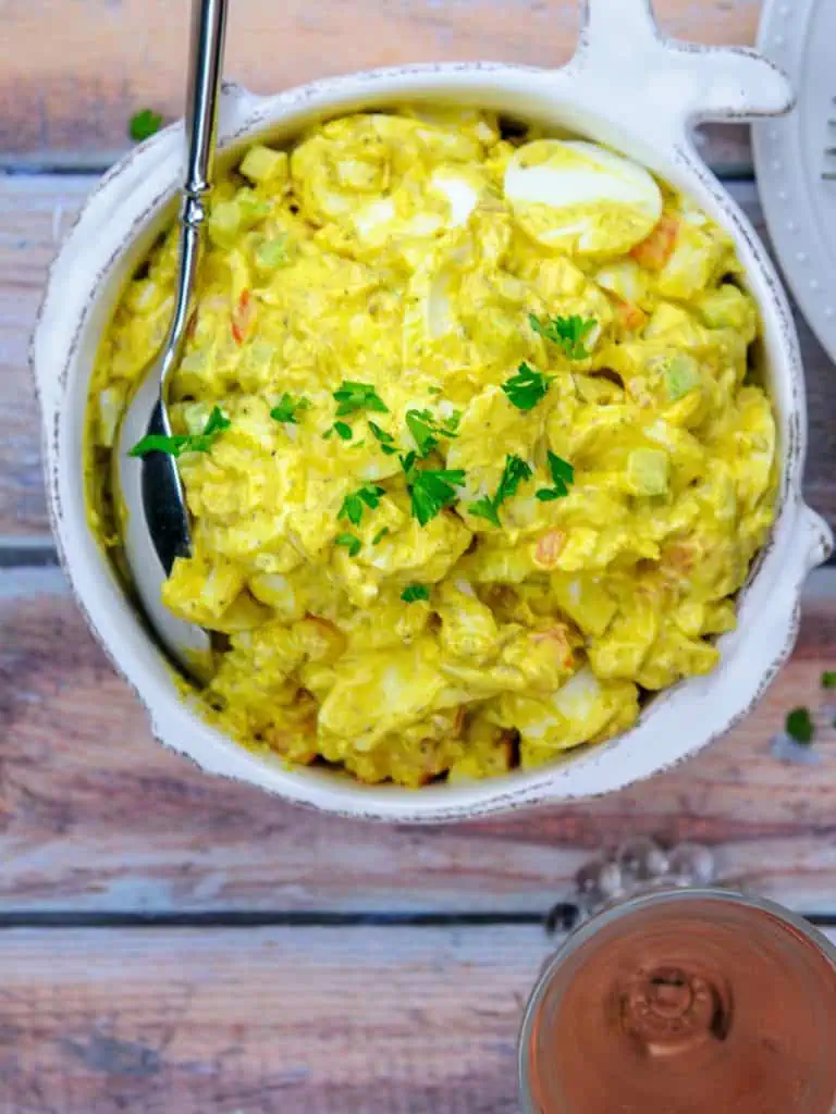 Overhead shot of a bowl of keto curried egg salad with a spoon, showcasing the vibrant yellow color and texture.