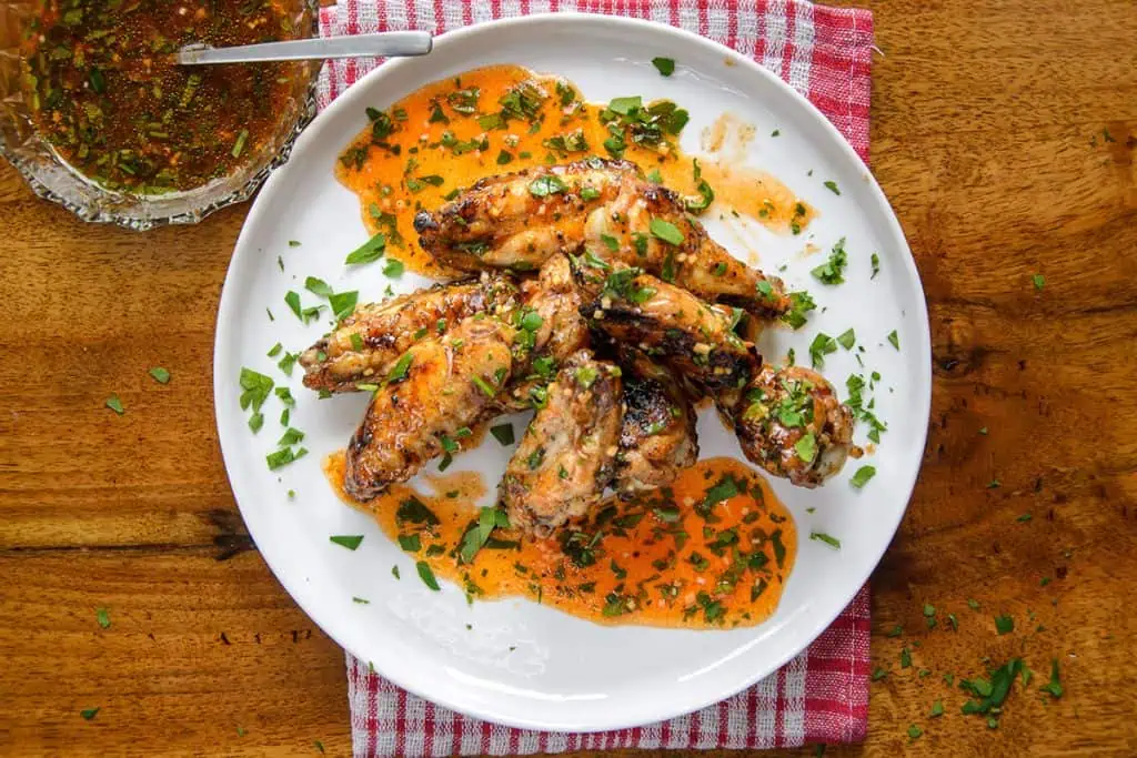 Lemon garlic chicken wings piled high on a white plate, drizzled with orange sauce and garnished with chopped parsley, set against a wooden table background.