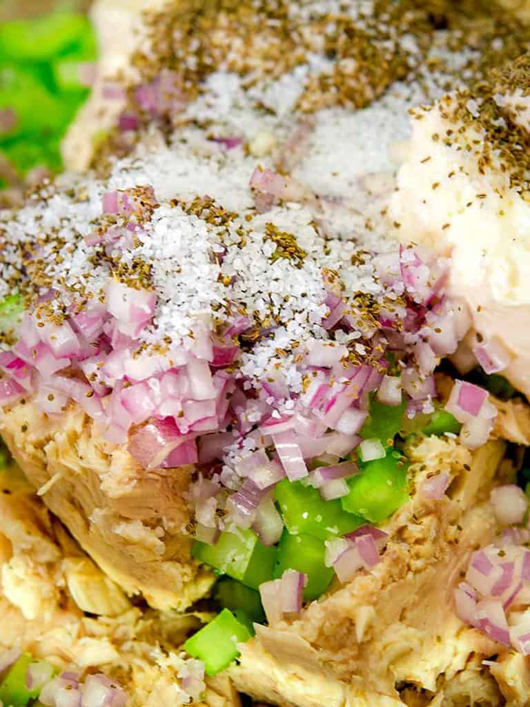 A bowl of low-carb tuna salad with diced celery and onions, placed on a textured surface with a spoon inside the bowl.