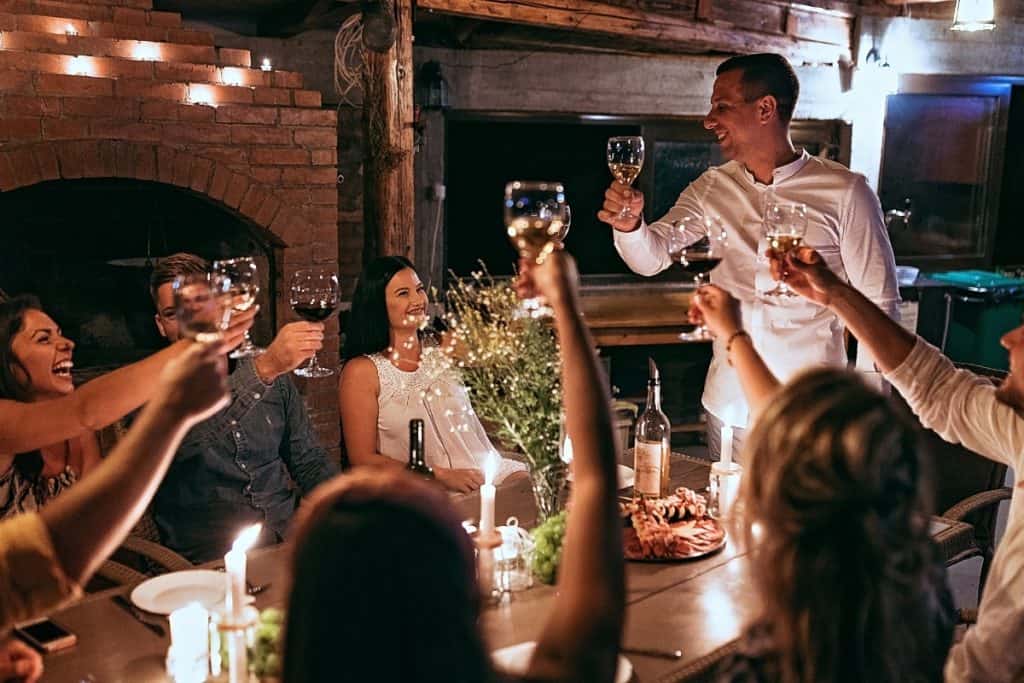 A group of friends raising their wine glasses in a toast during a cozy, festive dinner. The table is set with candles, plates of food, and wine bottles, creating a warm and joyful atmosphere.