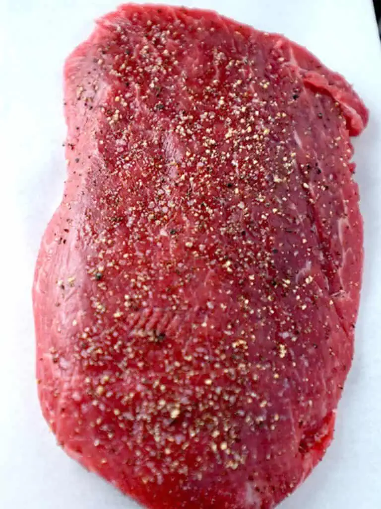 Raw flat iron steak seasoned with salt and pepper, ready for cooking.