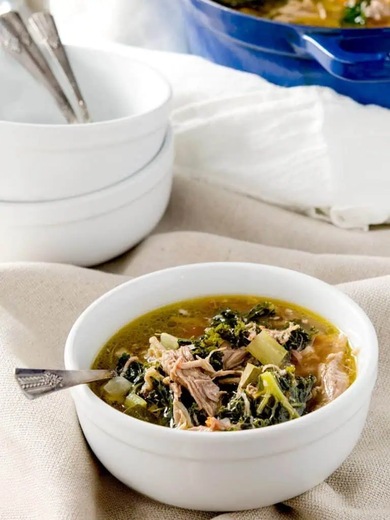A close-up view of a bowl of pulled pork soup, showcasing tender pieces of pork, kale, and vegetables in a savory broth.