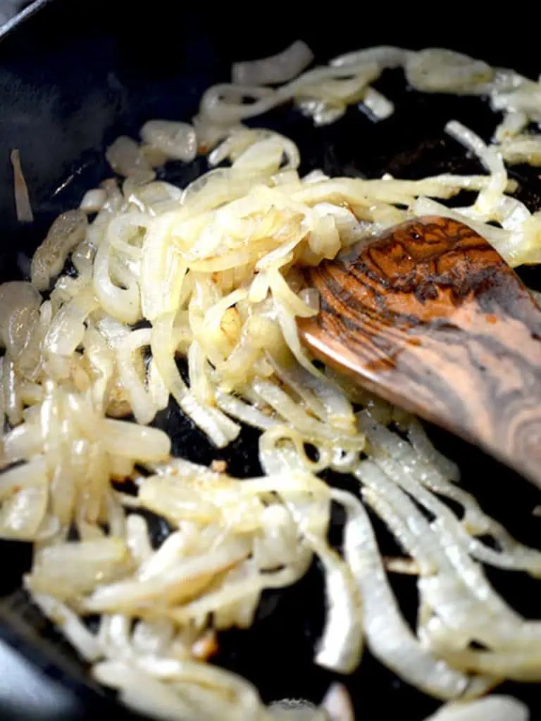 A close-up of caramelized onions being sautéed in a pan with a wooden spatula.