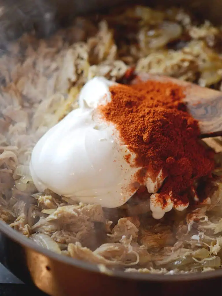 A mixture of shredded chicken, sautéed onions, sour cream, and paprika in a pan, ready to be mixed.