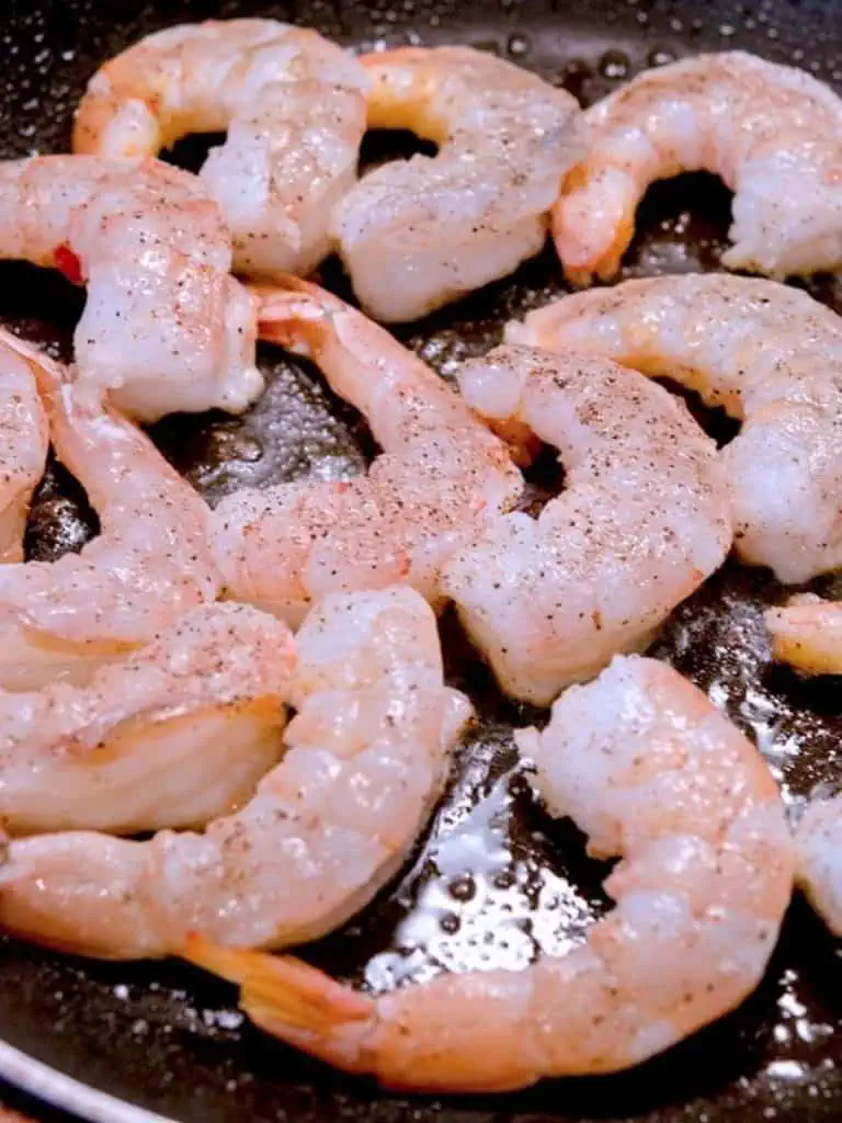 Seasoned shrimp being sautéed in a hot skillet, starting to turn pink and curl up.