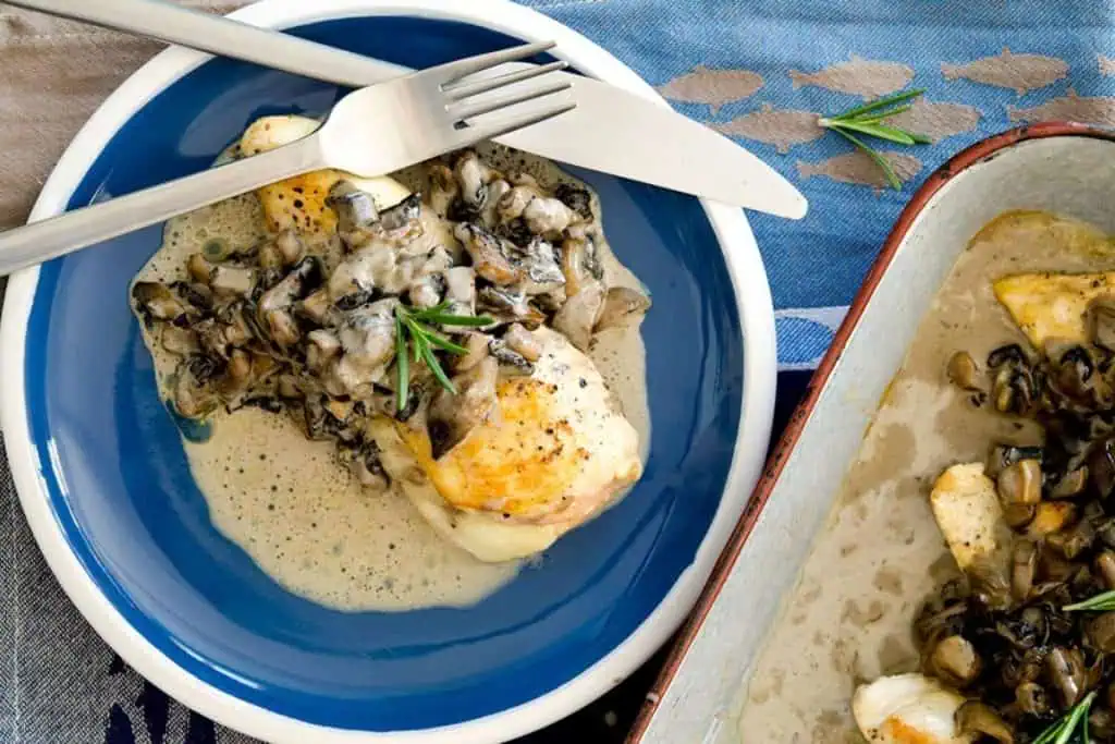 A close-up view of stuffed chicken breast topped with creamy mushroom gravy on a blue plate, garnished with a rosemary sprig.