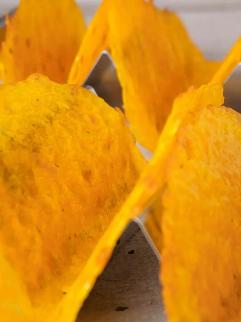 Close-up of cheese taco shells in a metal holder, showing detailed texture and crispy edges.
