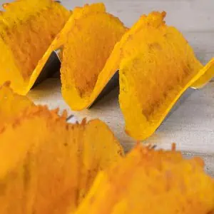 Close-up of cheese taco shells in a taco rack, showing their crispy texture and bright yellow color.