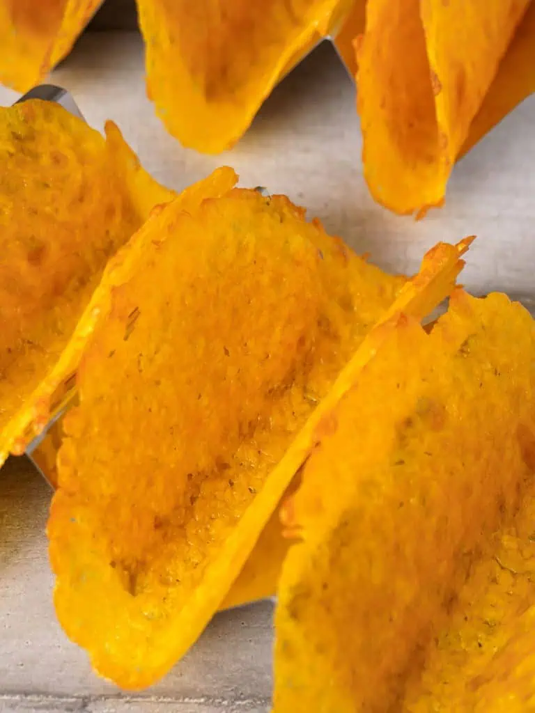 Rows of cheese taco shells in a metal holder, emphasizing their crispiness and vibrant golden hue.
