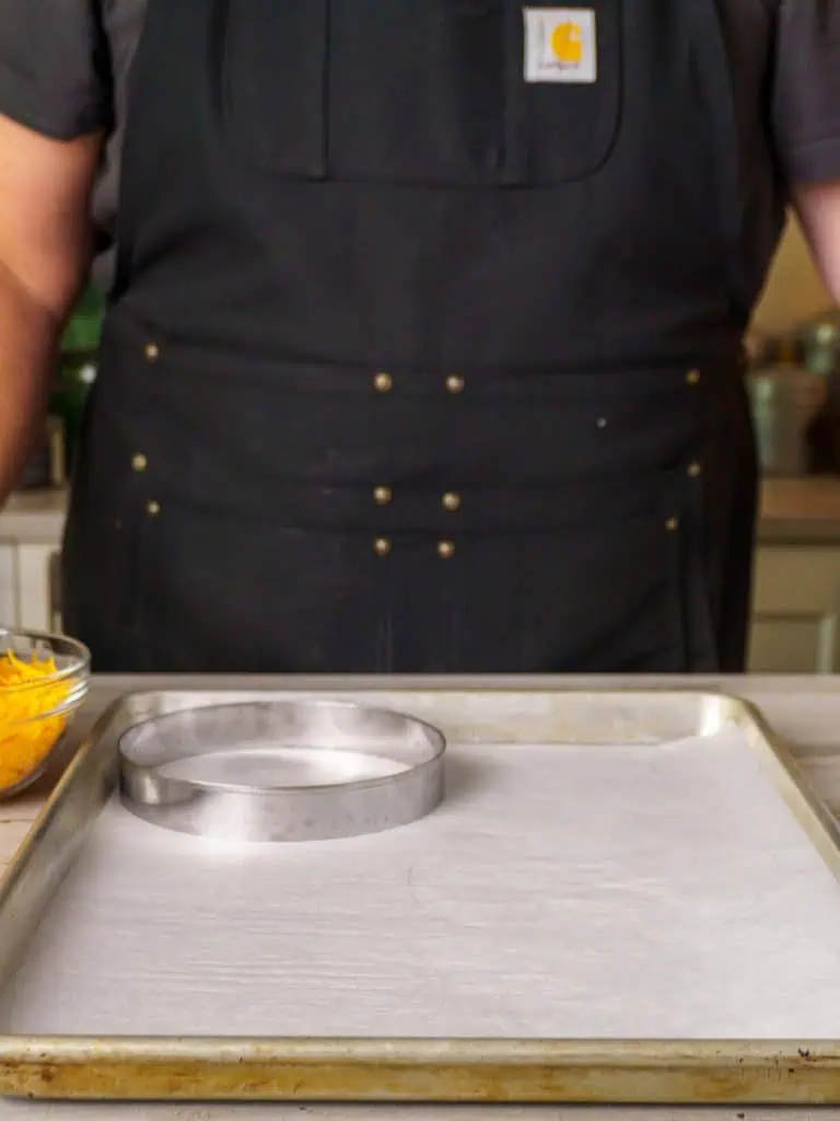 A baking sheet lined with parchment paper and a large metal ring placed on top, ready for shaping cheese taco shells.
