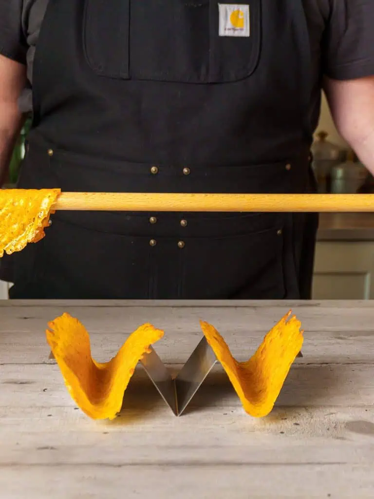 Two cheese taco shells placed on a metal taco stand after being shaped on the wooden dowel.