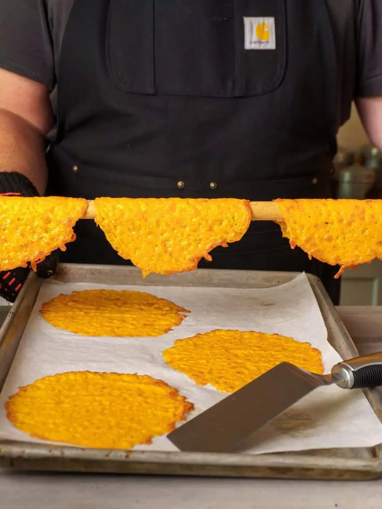 Melted cheese circles on the wooden dowel, placed above the parchment-lined baking sheet.