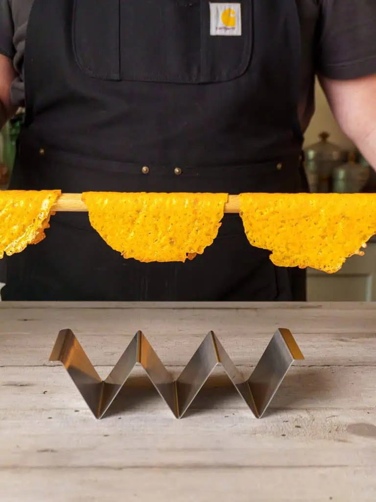 A close-up of the cheese taco shells draped over the wooden dowel, starting to harden into shape.