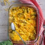 A close-up of a glass baking dish filled with Chicken and Broccoli Casserole, with a serving spoon digging into the cheesy and golden-brown casserole, showing a creamy and flavorful interior.
