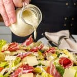 Pouring creamy Italian dressing over a colorful salad with various toppings.