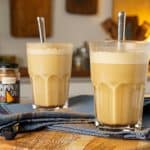 Two pumpkin spiced lattes in tall glasses with metal straws, set on a blue cloth with pumpkin pie spice sprinkled around.
