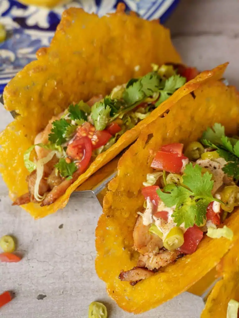 Close-up image of rotisserie chicken tacos filled with chopped chicken, tomatoes, and lettuce, served in cheese shells with a sprinkle of fresh cilantro.