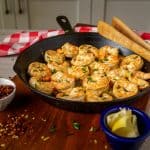 Sautéed shrimp garnished with chives in a black skillet.
