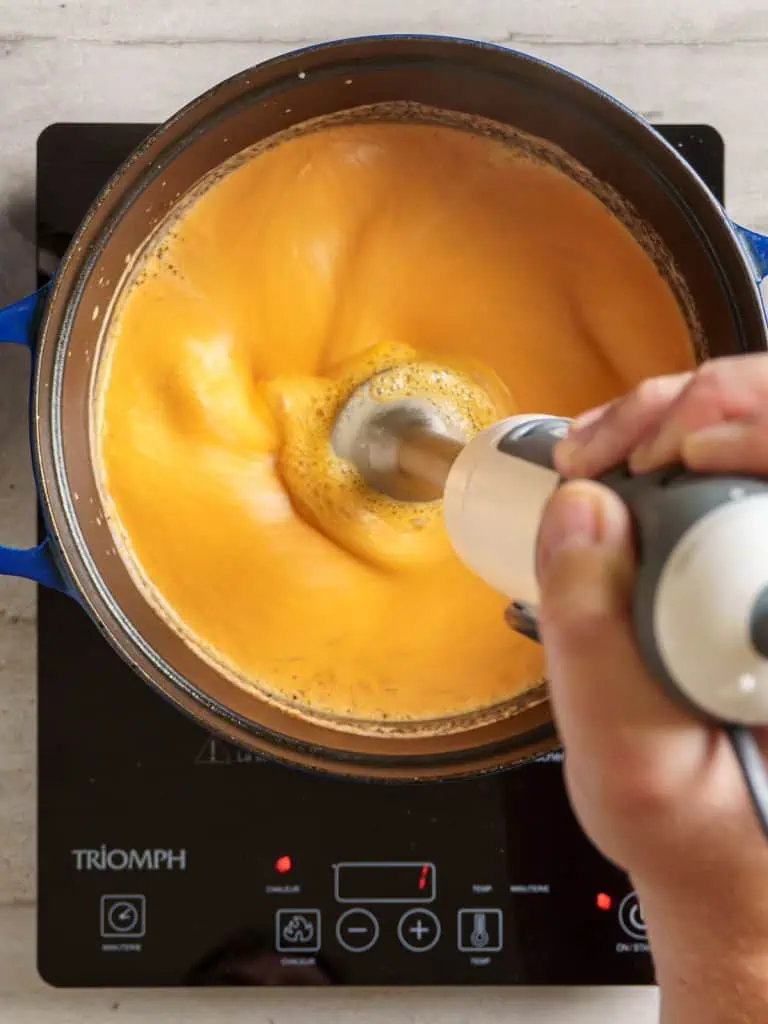 Blending the tomato bisque with an immersion blender to create a smooth texture.