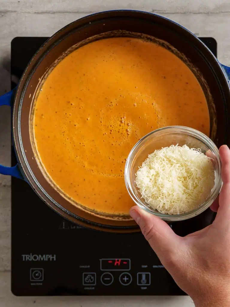 Adding grated Parmesan cheese into the blended tomato bisque.