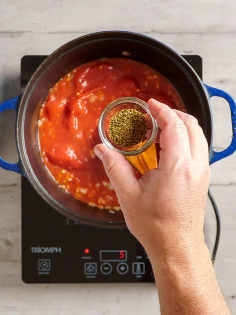 Sprinkling dried oregano into the tomato and onion mixture.
