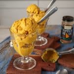 Glass cup filled with creamy pumpkin ice cream, with a jar of pumpkin spice in the background, set on a rustic wooden surface.